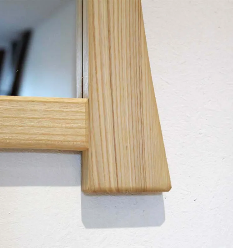Angle inférieur d'un miroir en bois au design asymétrique avec encadrement débordant.