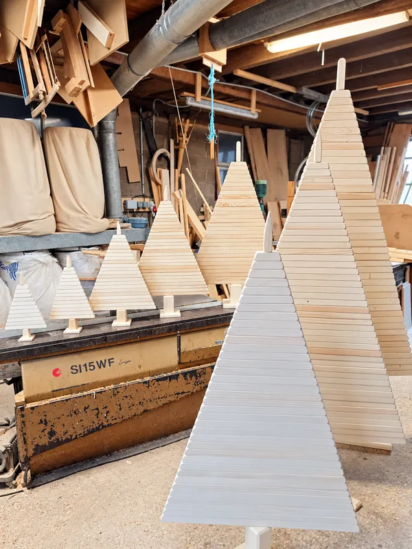 Différentes tailles de sapins de Noël en bois artisanaux présentées dans l’atelier Les Petits Copeaux